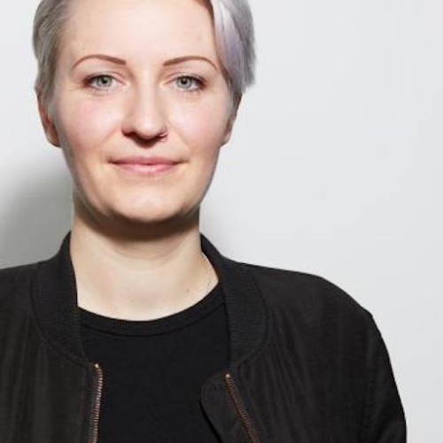 Profile picture of Kathy Meßmer, with short white hair and dressed in black.